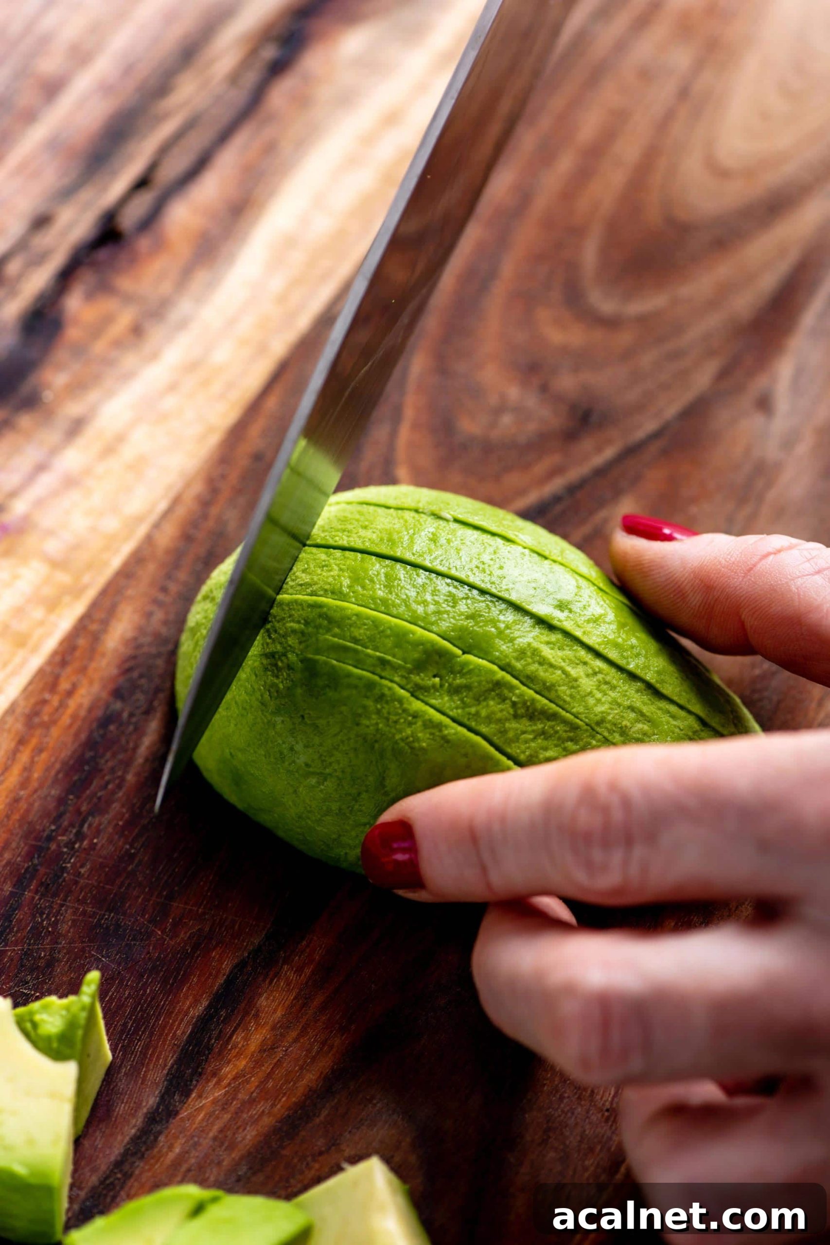 Woman slicing avocado on cutting board.