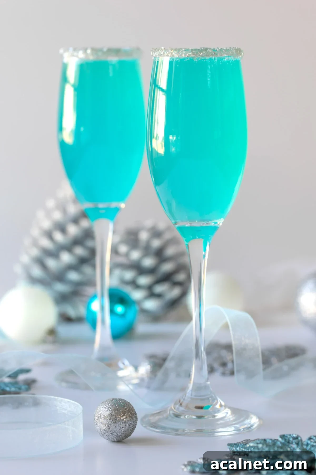 Two champagne flutes filled with turquoise Tiffany mimosas that are rimmed with silver edible glitter.