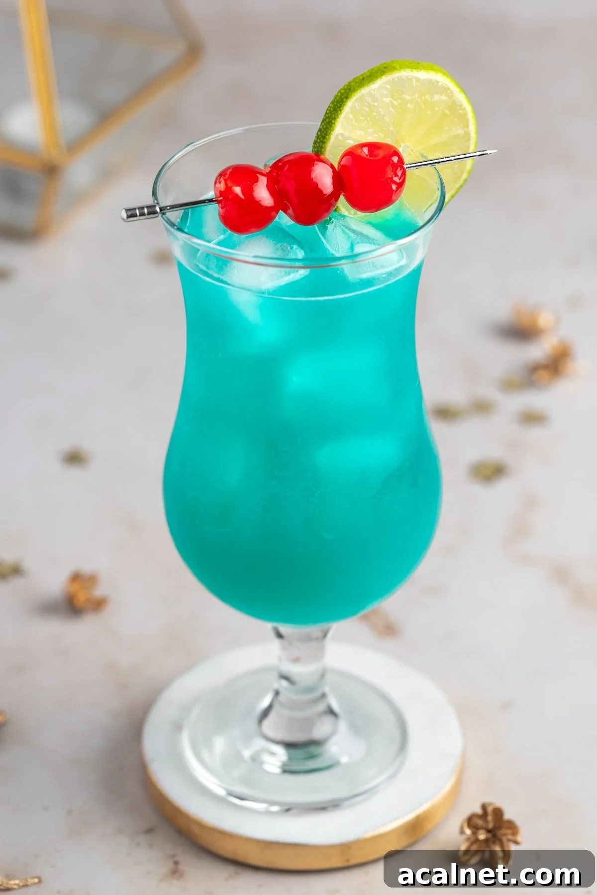 A tall hurricane glass filled with blue liquid and ice. Garnished with three maraschino cherries on a skewer and a lime wheel.