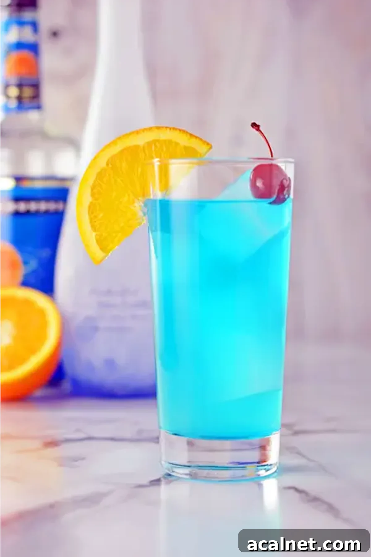 A neon blue cocktail on the rocks in a tall glass. Garnished with an orange slice and a maraschino cherry.