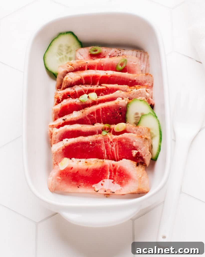Spring onions and cucumber slices top sliced air-fried tuna steak on a rectangular dish.