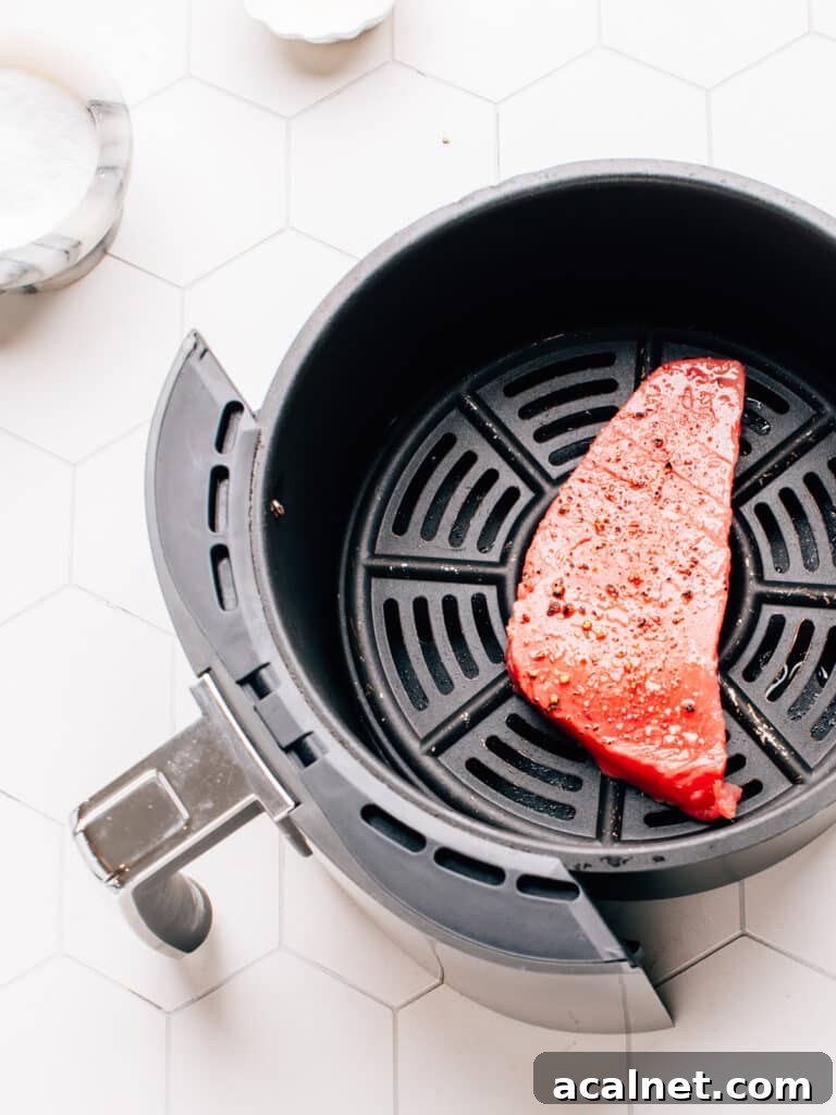 Raw ahi tuna steak in the air fryer basket with salt and pepper.