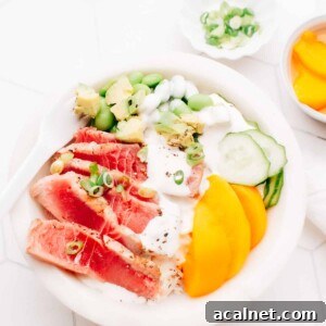 Sliced seared air fryer tuna in a poke bowl with peach slices, edamame, cucumber and green onions, drizzled with sauce.