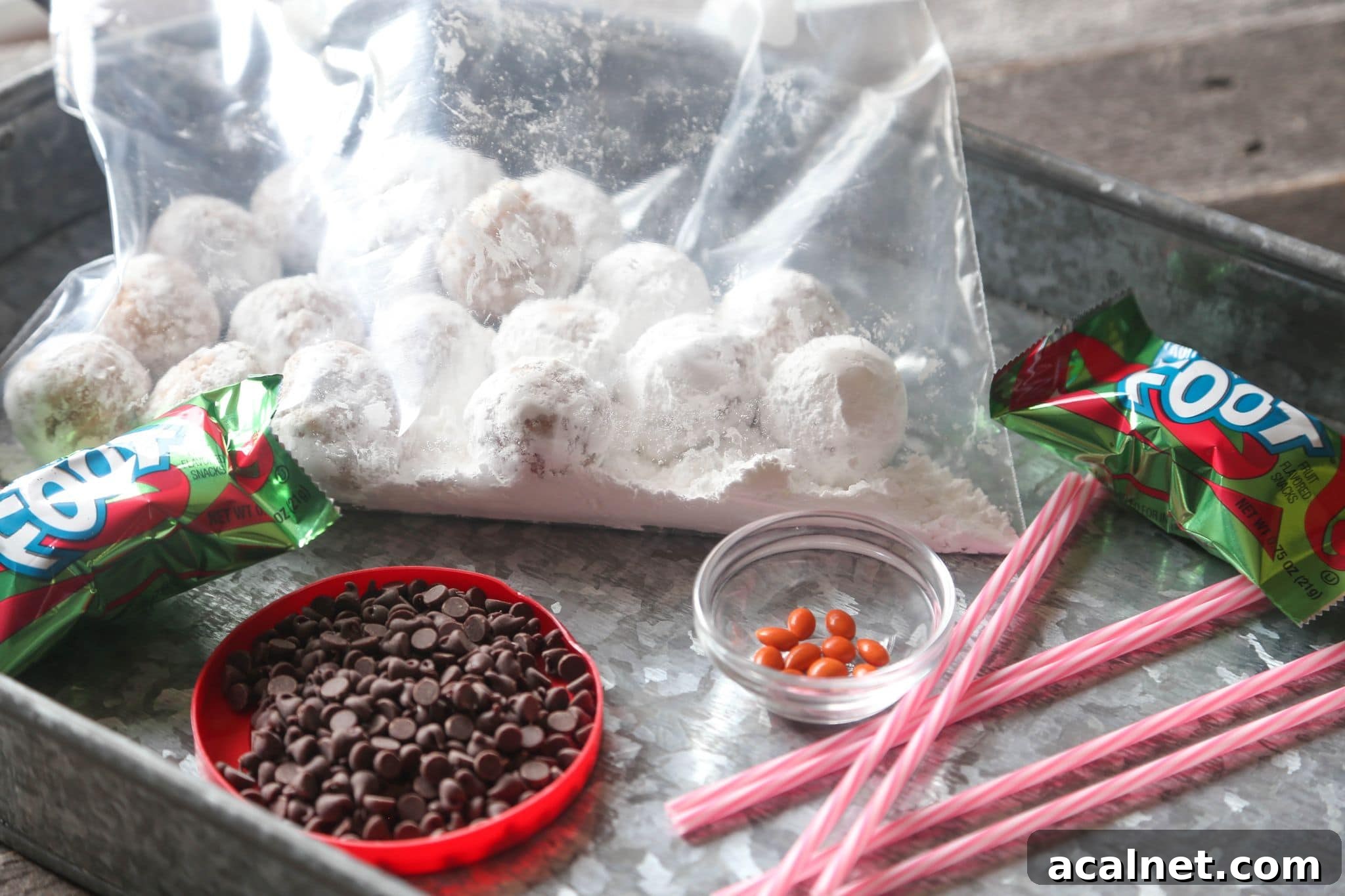 This easy snowman cake tutorial turns a chocolate layer cake into a winter wonderland, topped with adorable snowmen made from mini donuts! Supplies needed to decorate a snowman cake, including a bag of powdered donut holes, chocolate chips, and cake pop sticks.