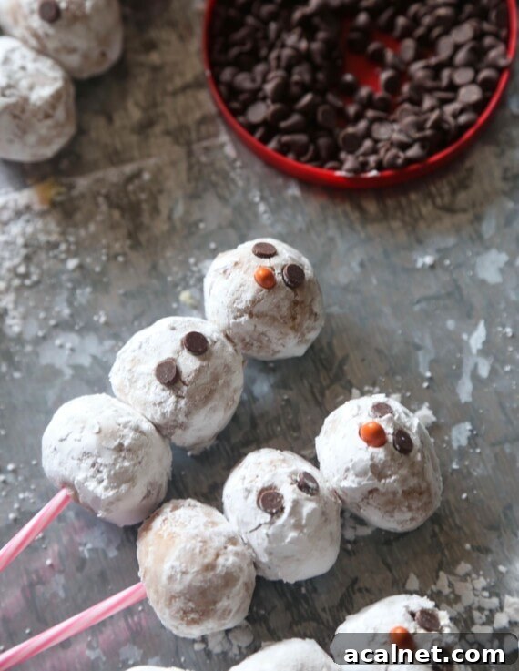 Add the eyes, nose, and buttons. Three snowman cake pops on sticks with chocolate chips as the eyes and buttons.