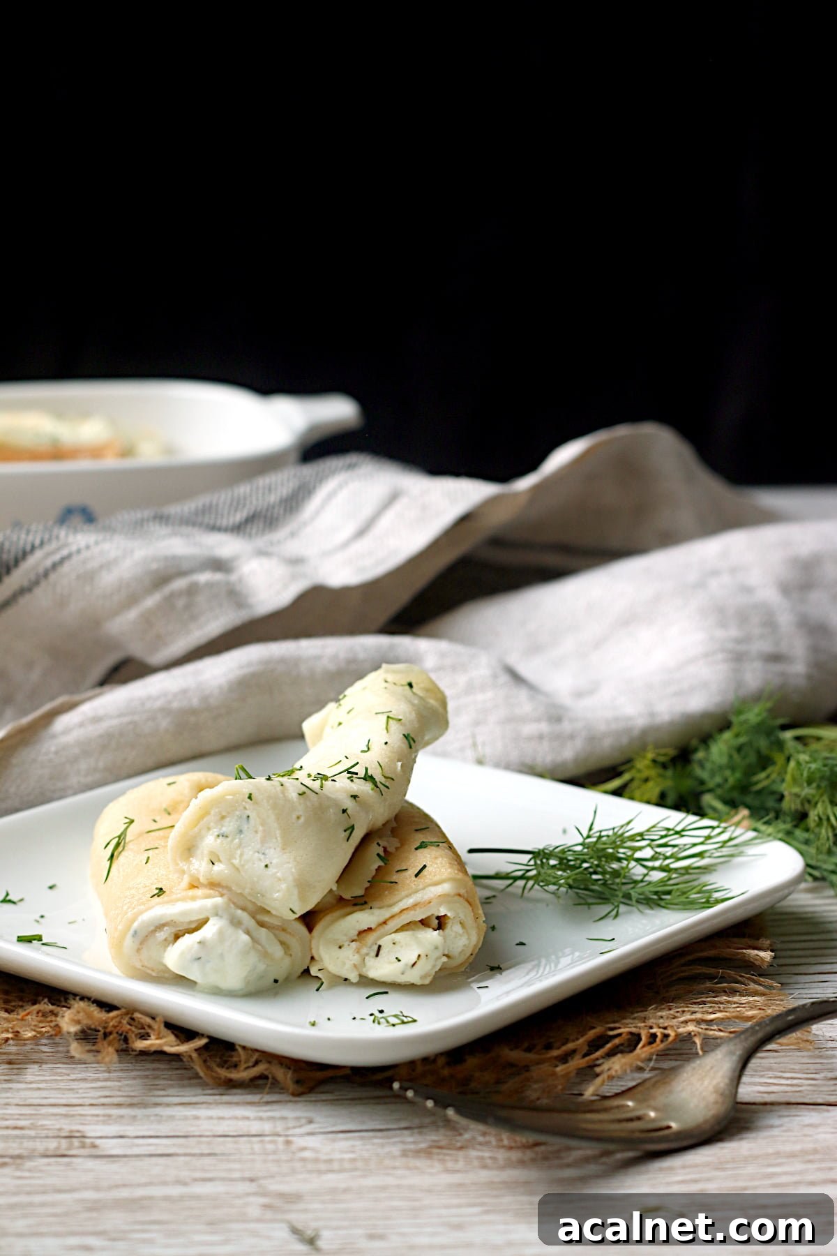 Nalysnyky (Savory Ukrainian Crepes with Dill and Cottage Cheese) on a small, square, white plate.