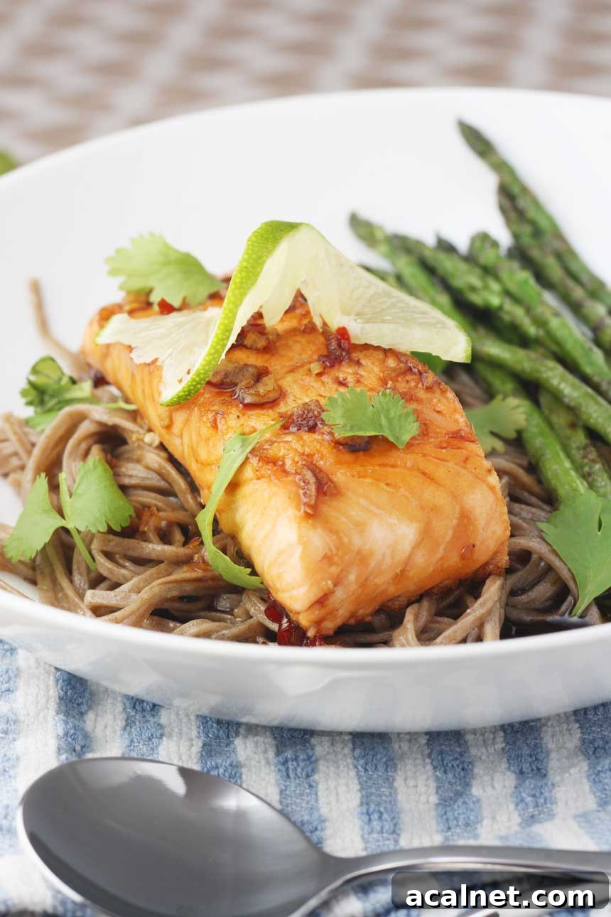 A closeup of a white dish of maple teriyaki salmon with soba noodles and asparagus.