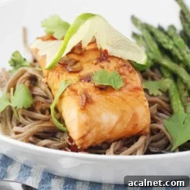 A white dish with maple teriyaki salmon with soba noodles in it.