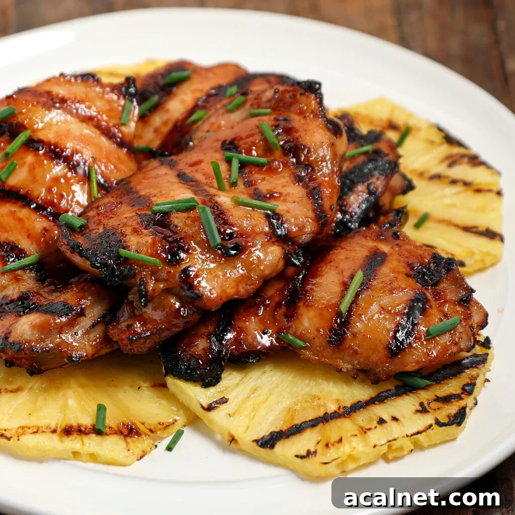 Grilled huli huli chicken thighs glazed and garnished with chopped chives, served atop grilled pineapple slices on a white plate.