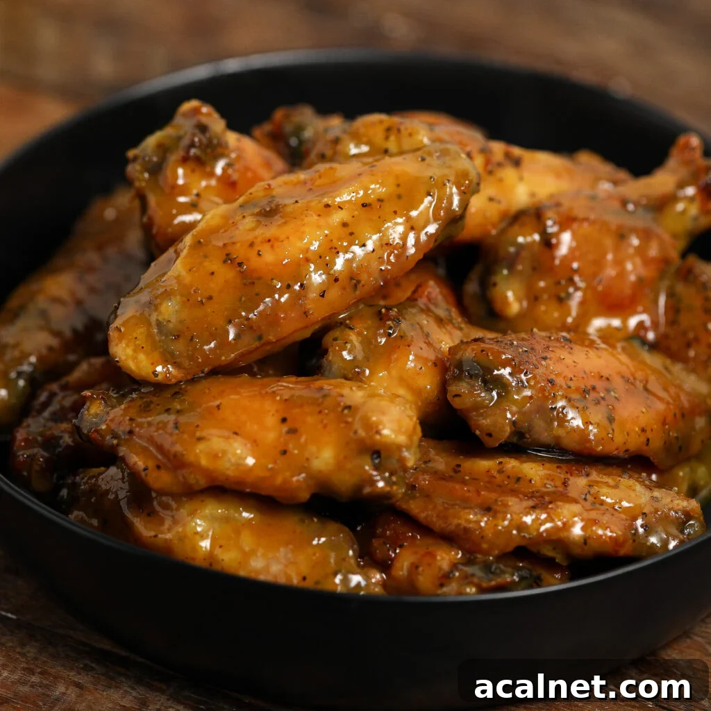 A black bowl filled with Carolina Mustard BBQ Chicken Wings, glazed in a shiny, seasoned sauce and placed on a wooden surface.