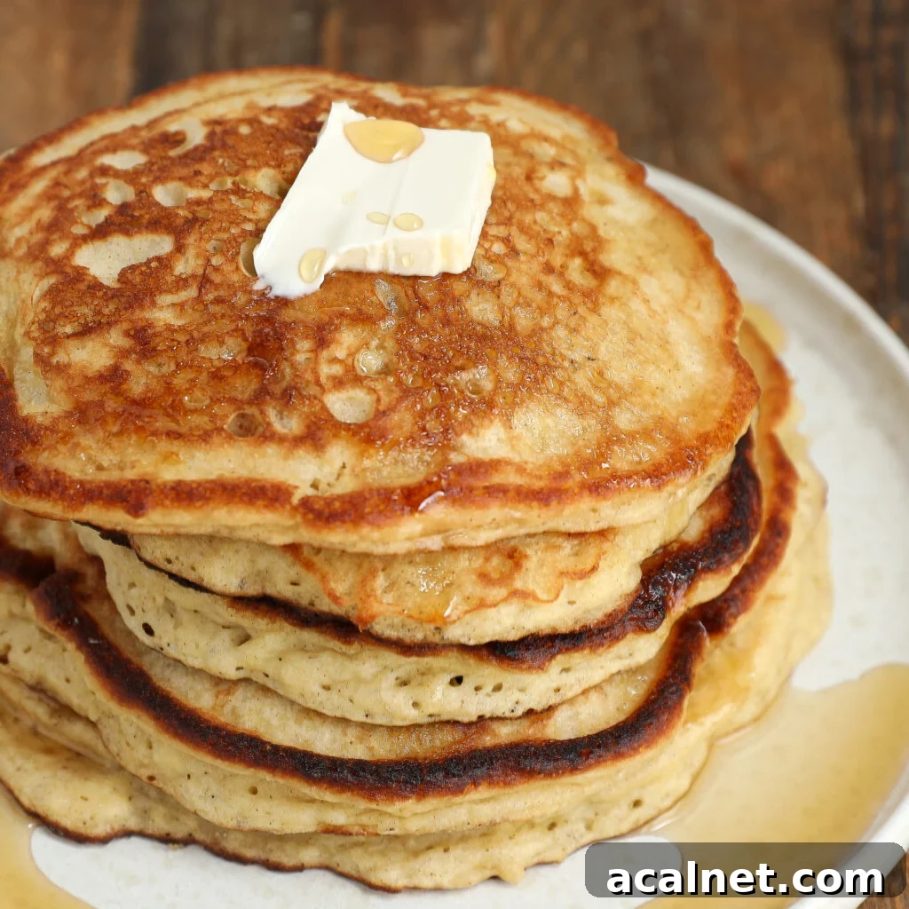 A stack of golden-brown, fluffy banana pancakes topped with a square of butter and drizzled with syrup, served on a white plate on a wooden table.
