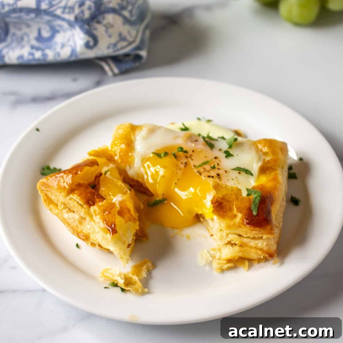 A baked egg in a puff pastry shell with the yolk running on the plate.