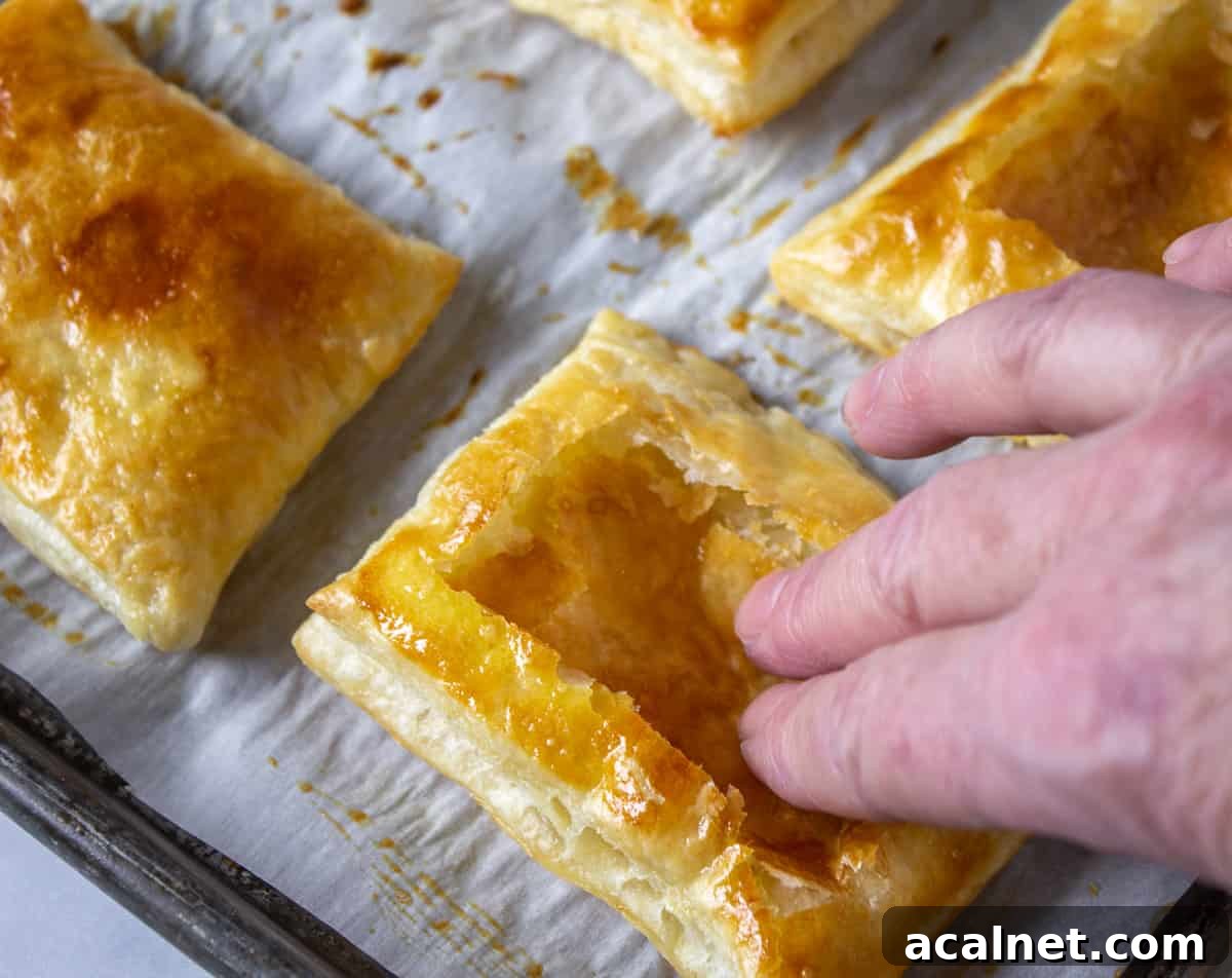 Finger tips pushing down the center of a puff pastry shell.