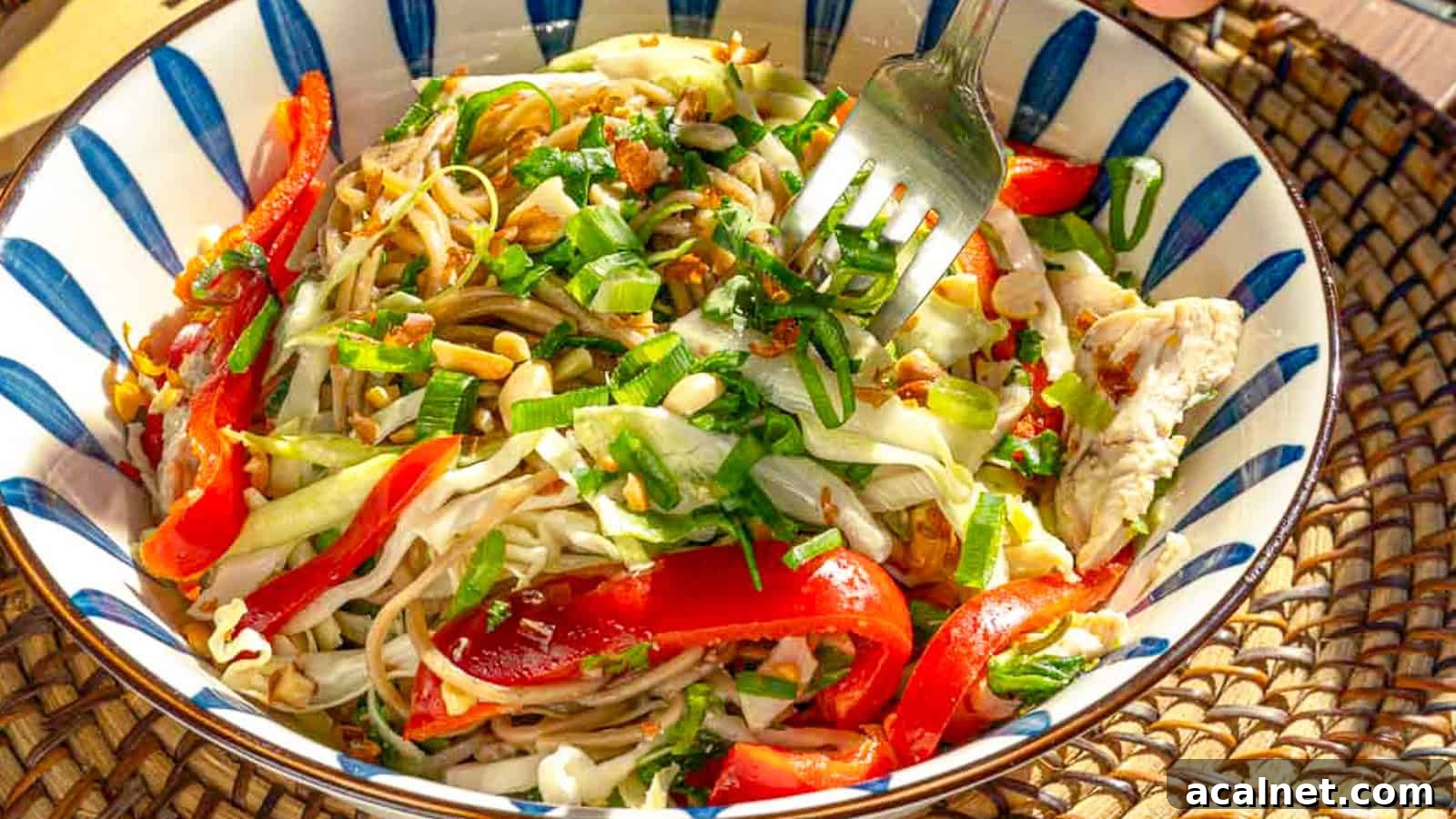 29 Chicken Dinners That Keep Coming Back to Our Weekly Menu 23 A colorful salad in a striped bowl, featuring mixed vegetables such as red bell peppers and shredded cabbage, garnished with crushed nuts and fresh herbs. A fork is seen lifting a portion, emphasizing the dish's vibrant, fresh ingredients.