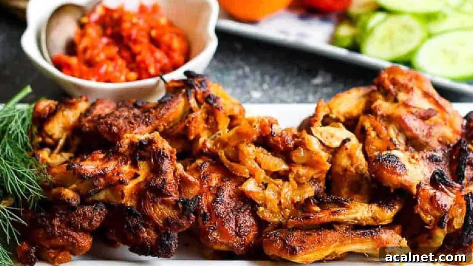 29 Chicken Dinners That Keep Coming Back to Our Weekly Menu 24 Low angle shot of chicken shawarma on a white platter with harissa paste and tomatoes and cucumbers in the background.