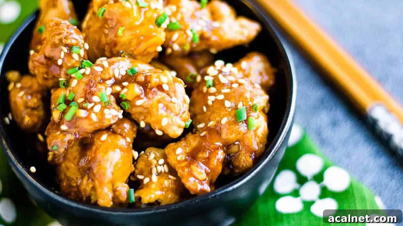29 Chicken Dinners That Keep Coming Back to Our Weekly Menu 27 Fried chicken pieces in orange sauce garnished with sesame seeds in a black bowl with chopsticks and a green and white napkin.