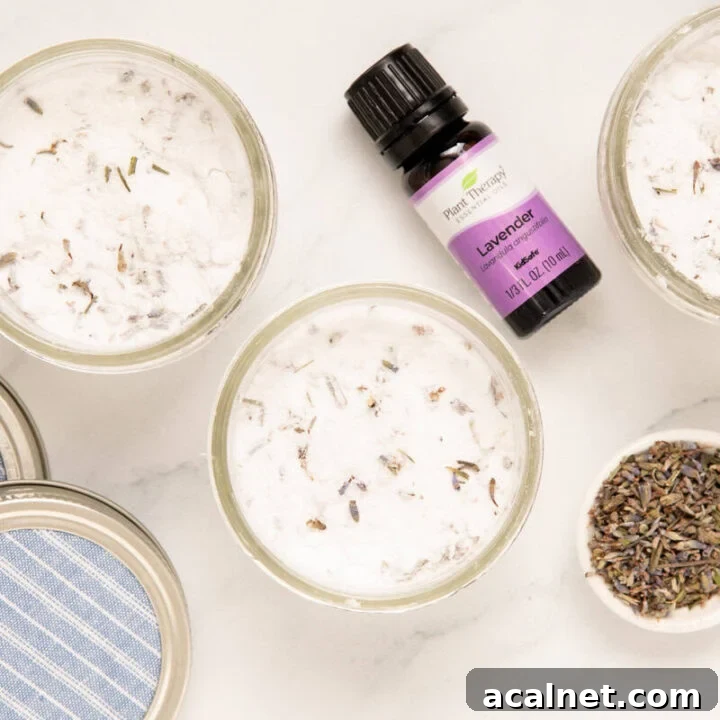 mason jars of homemade air freshener with a bottle of lavender essential oil and a spoonful of lavender buds next to it