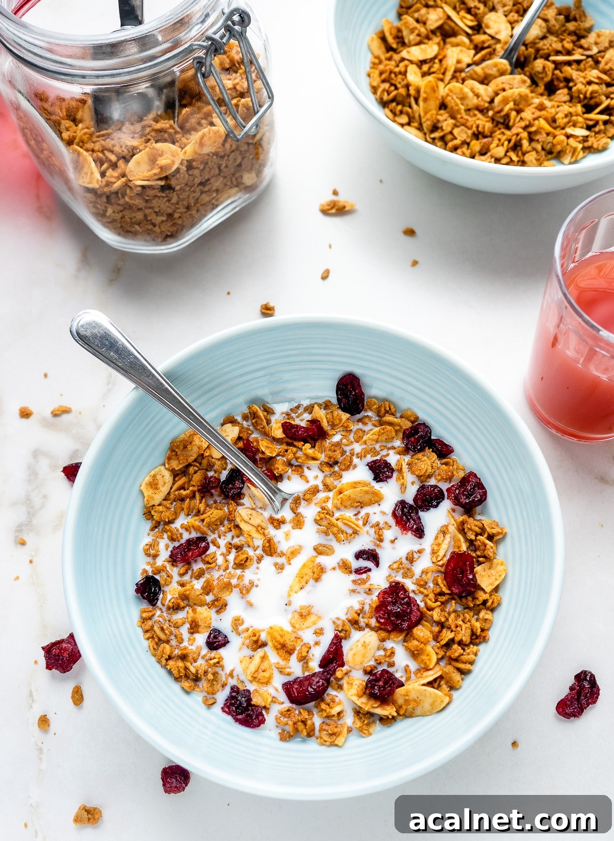Bowl of French vanilla almond granola with milk and a glass of juice next to it.
