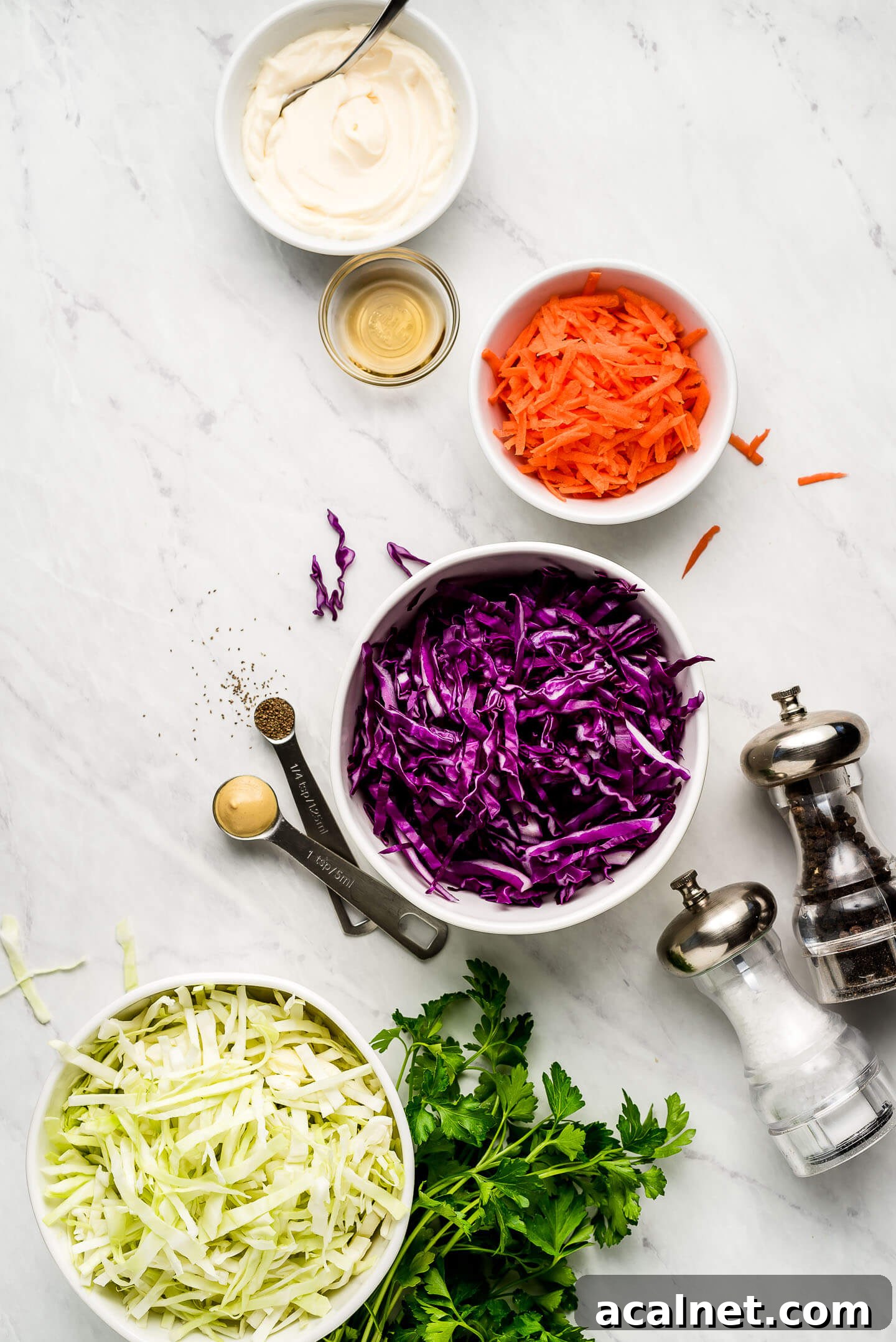Ingredients on a marble surface- mayonnaise, vinegar, shredded carrots, red and green cabbage, and parsley.