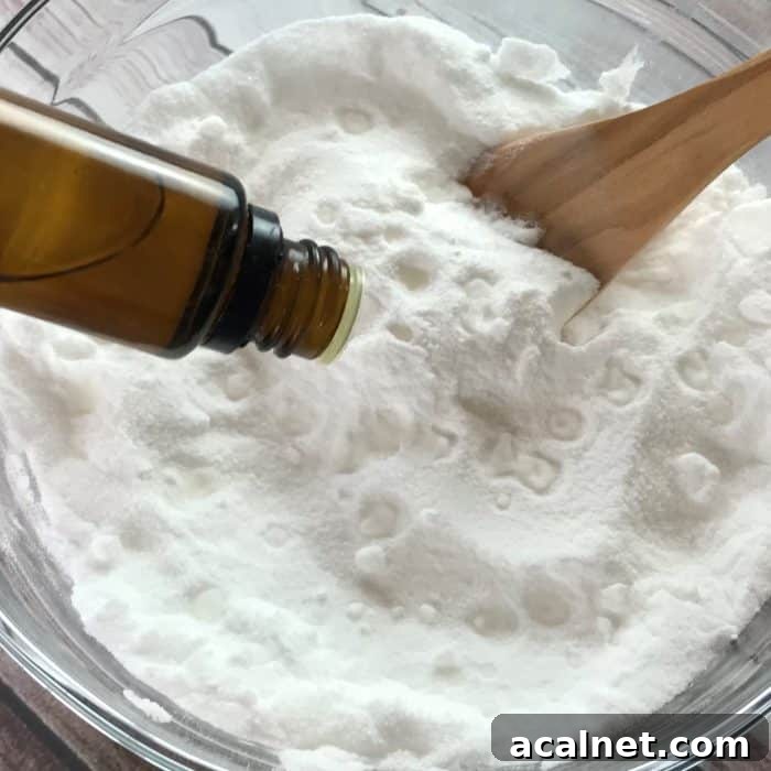 adding drops tea tree essential oil from essential oil bottle to baking soda and citric acid in glass bowl for making essential oil facial steamer tabs