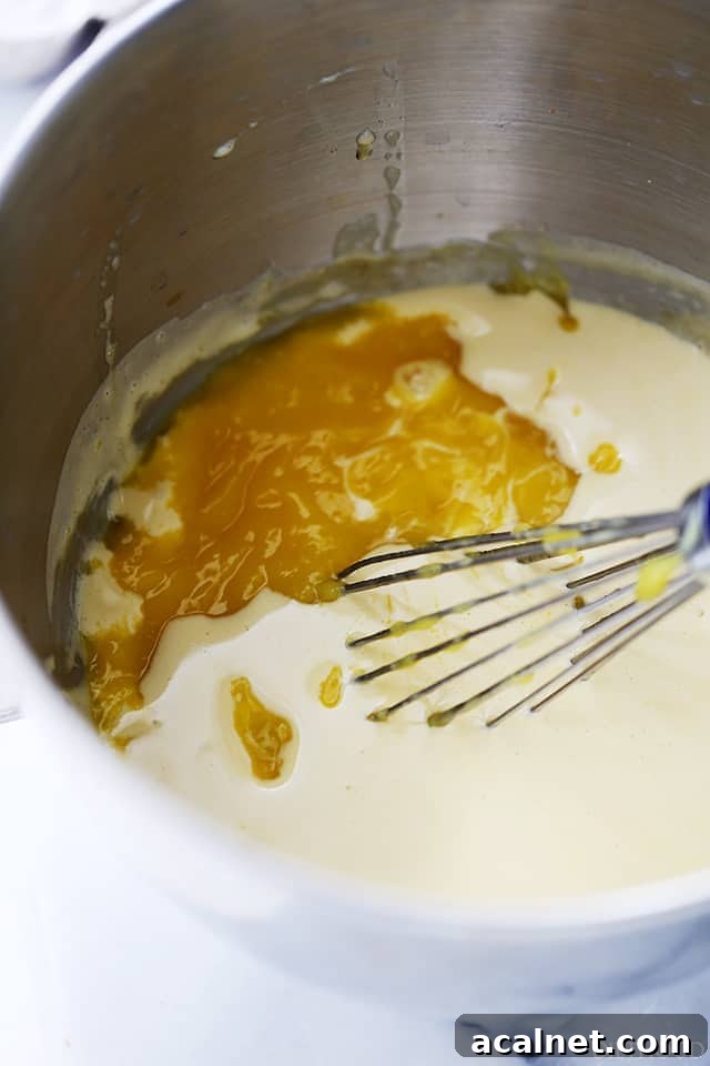 Pureed mangoes being mixed with zabaglione in a large metal bowl.