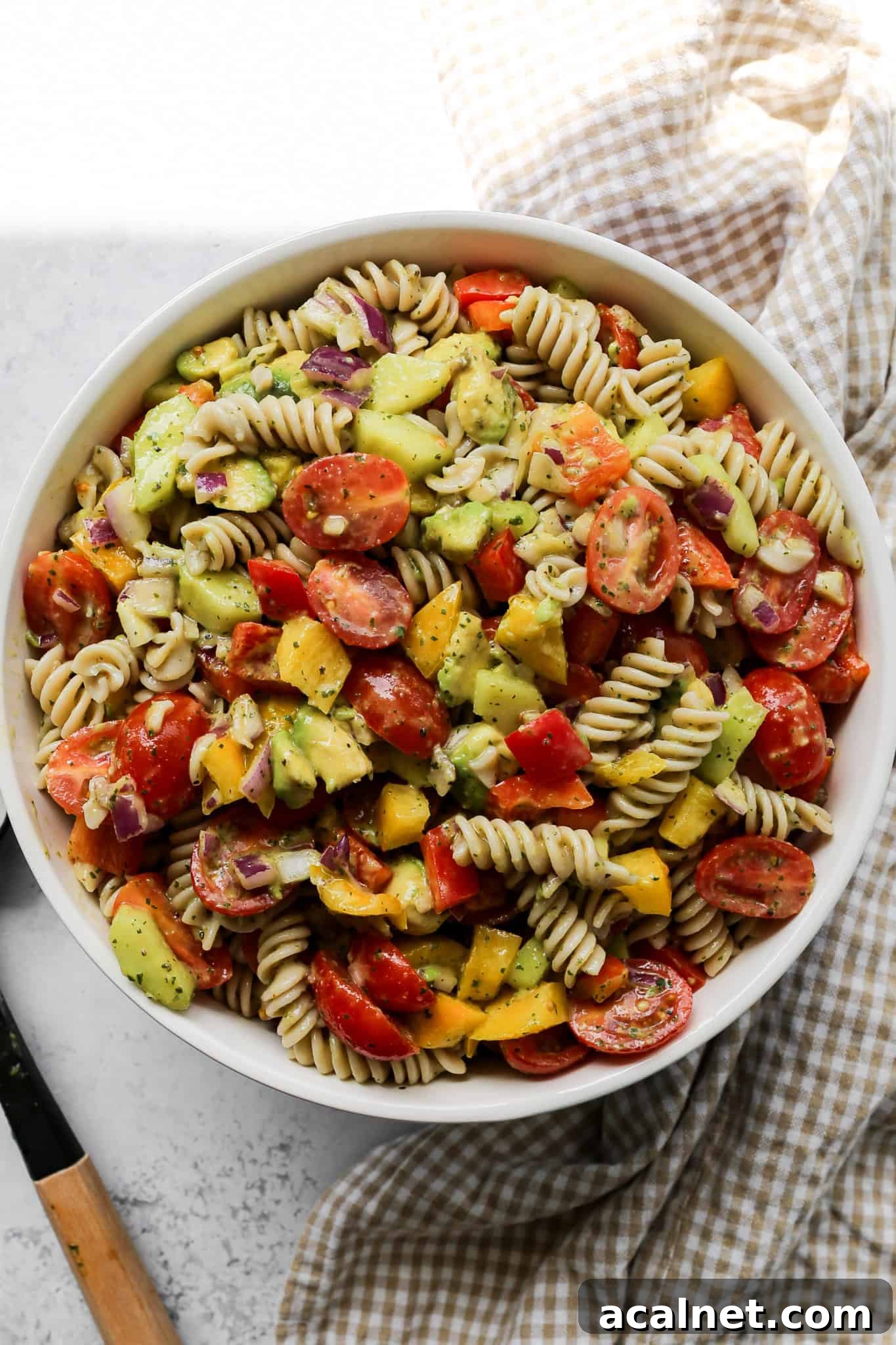 a serving bowl of gluten free lime cilantro pasta salad next to a serving spoon and a tan gingham kitchen towel