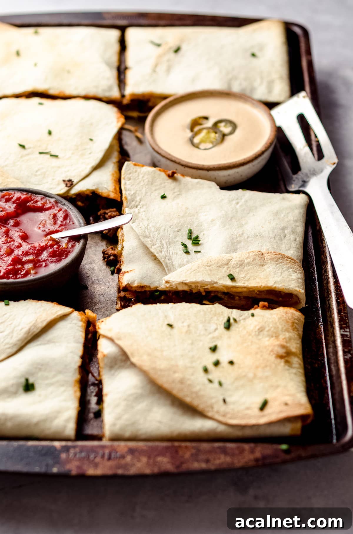 Sheet Pan Quesadillas: Quick Oven-Baked Mexican Dinner 2 A sheet pan filled with square quesadillas, and small bowls of queso and salsa.