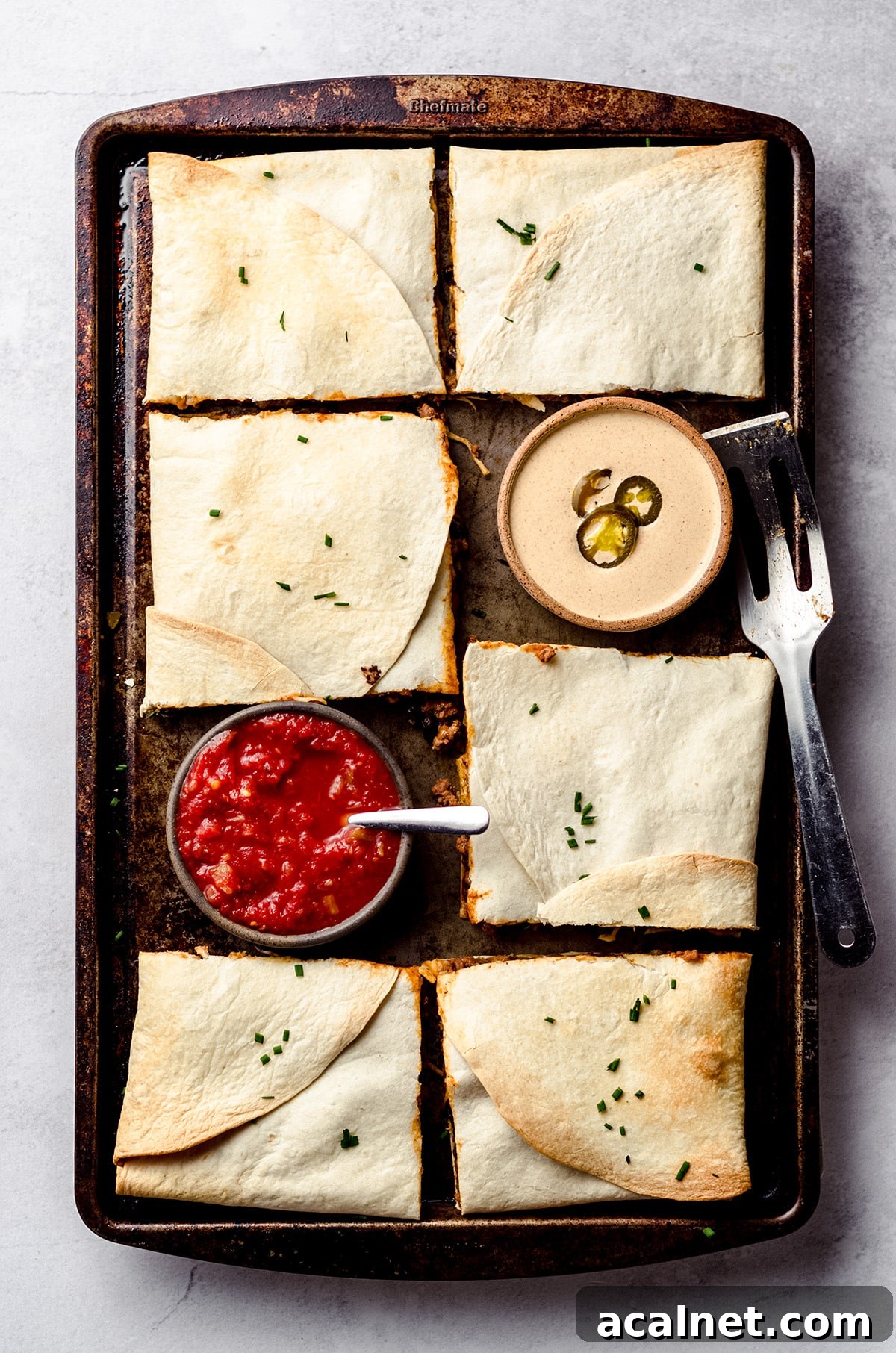 Sheet Pan Quesadillas: Quick Oven-Baked Mexican Dinner 16 An overhead shot of a sheet pan filled with square quesadillas and served with bowls of sauce and salsa.