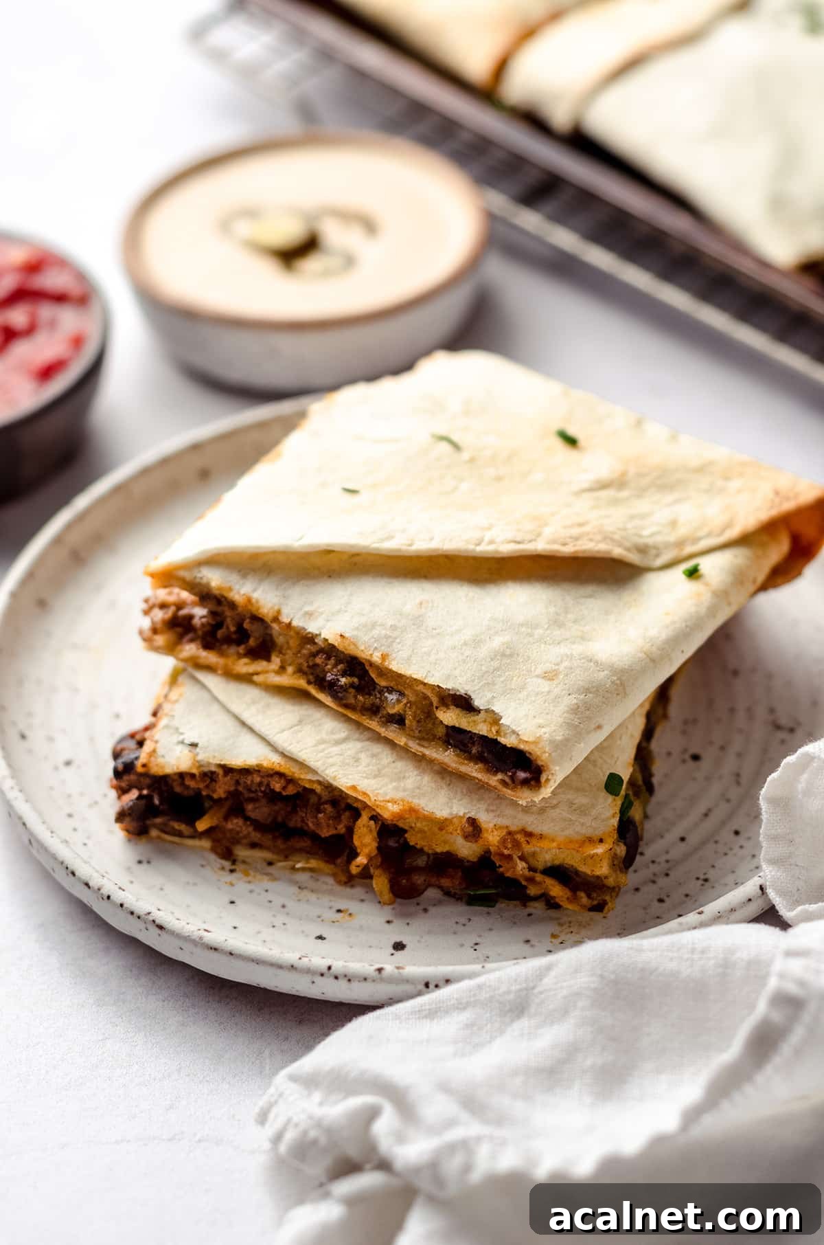 Sheet Pan Quesadillas: Quick Oven-Baked Mexican Dinner 4 Two squares of quesadilla with bowls of sauce in the background.