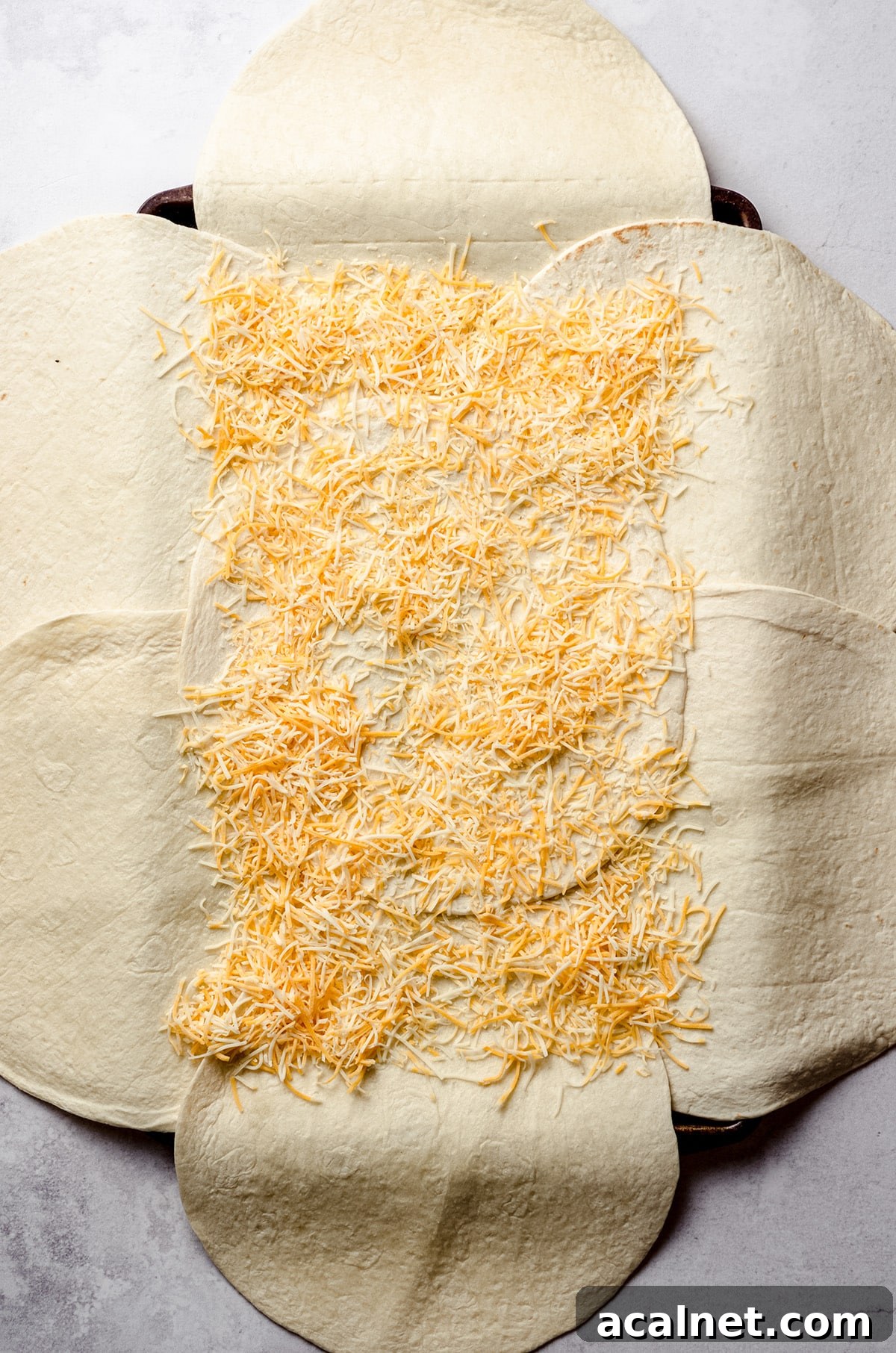 Sheet Pan Quesadillas: Quick Oven-Baked Mexican Dinner 10 Adding shredded cheese to a sheet pan layered with tortillas.