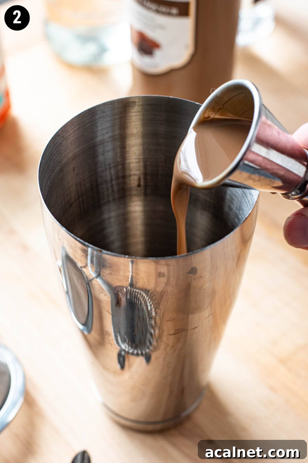 A double jigger pouring chocolate liqueur into a cocktail shaker.