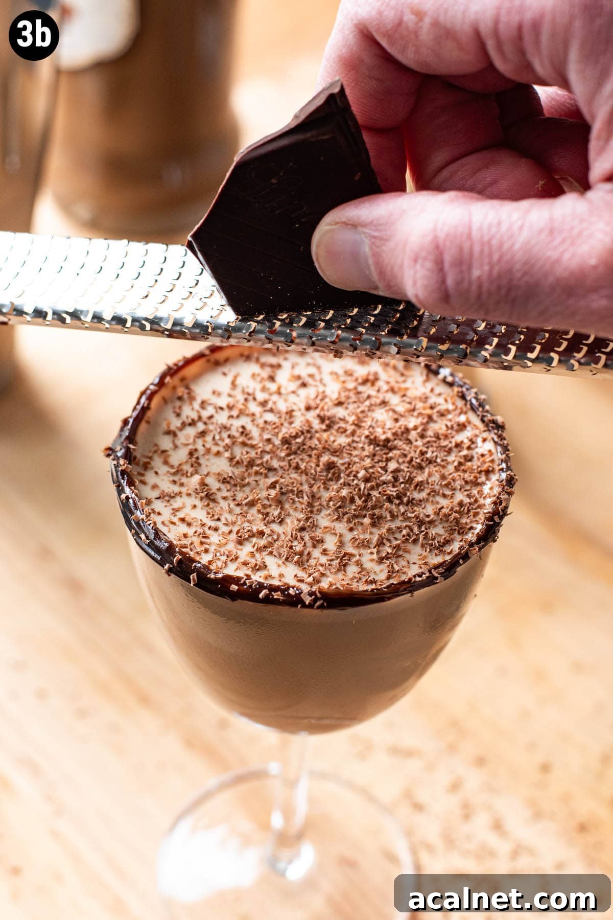 A hand grating a chunk of chocolate over the top of a chocolate martini.