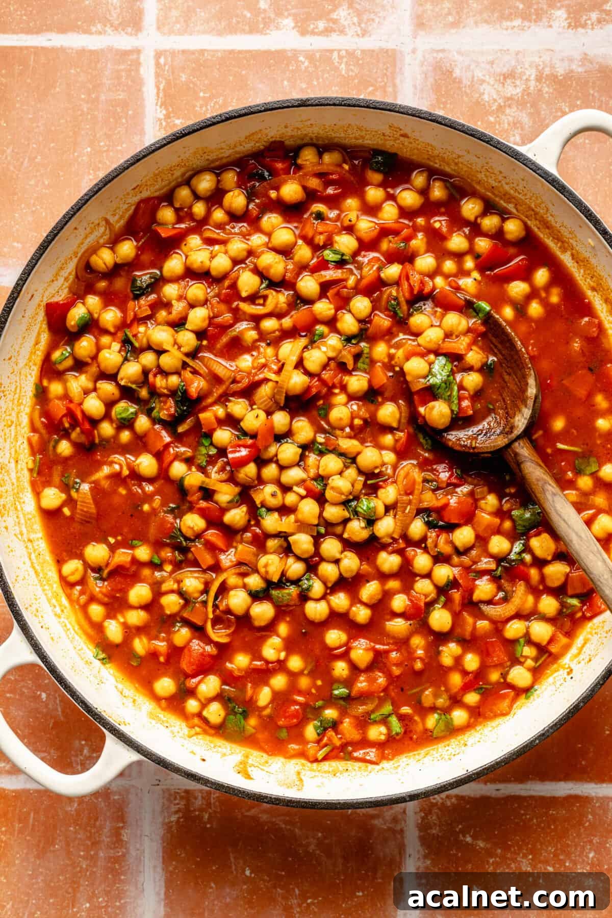 Chickpeas simmering in broth in a white skillet.