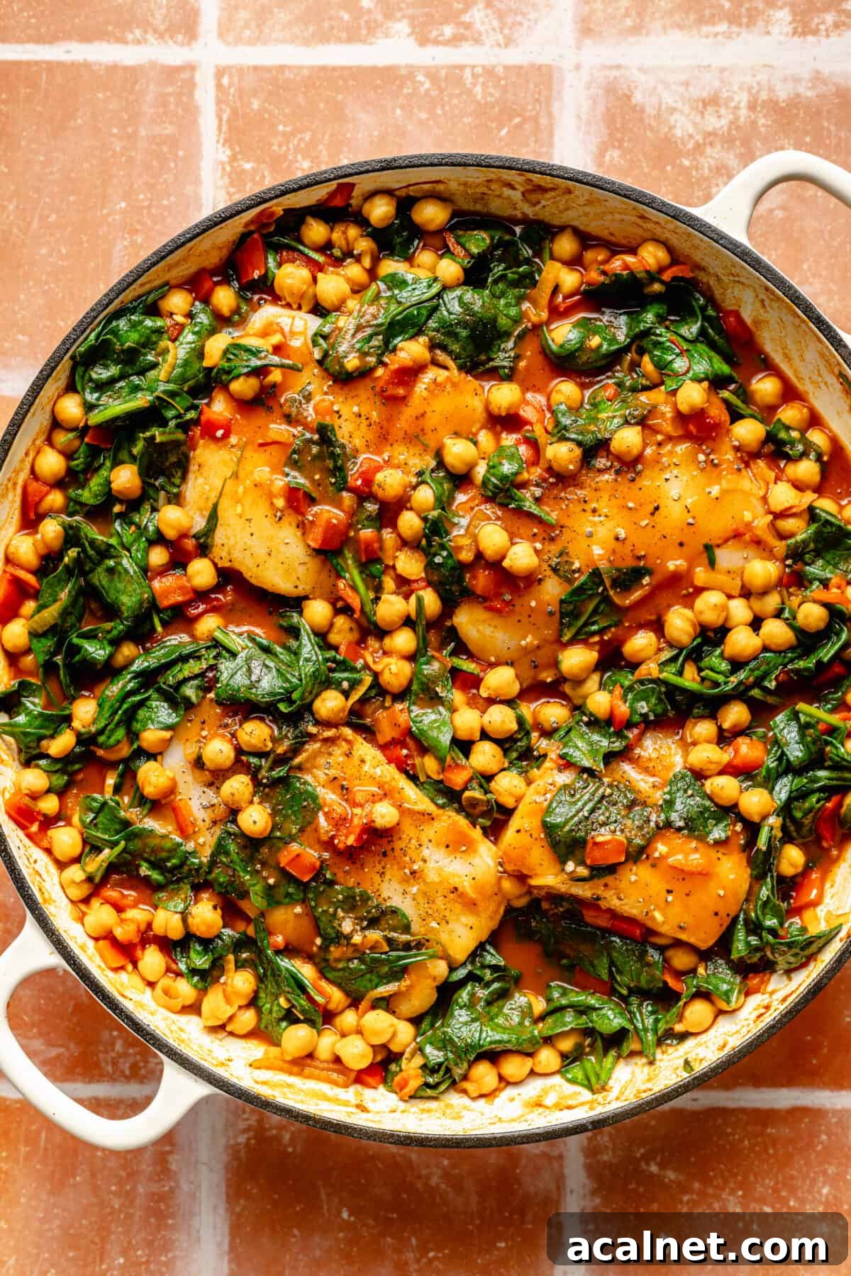 Spanish-Inspired Simmered White Fish in skillet. Fish and spinach added.