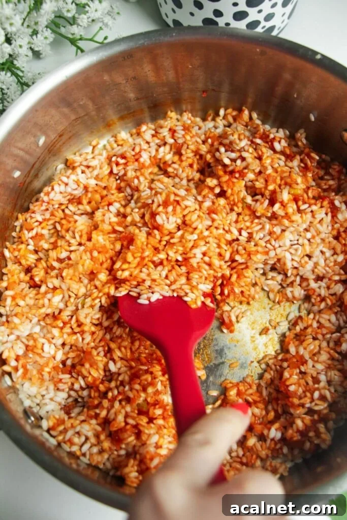 Gochujang Cheesy Risotto with Creamy Korean Chili Flavor 7 Rice added to a large pan, being stirred with a spatula.