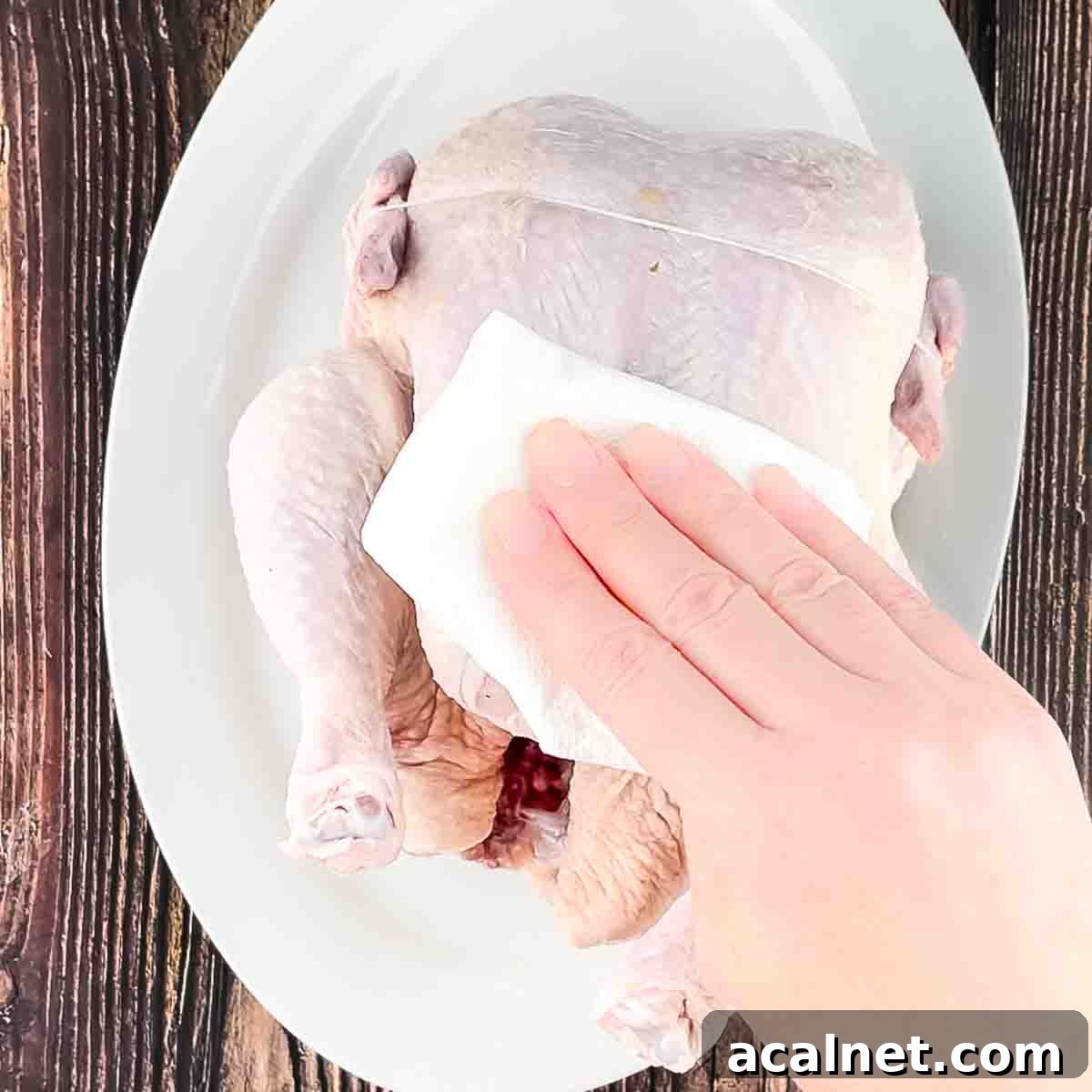 A hand patting the chicken dry with a paper towel.