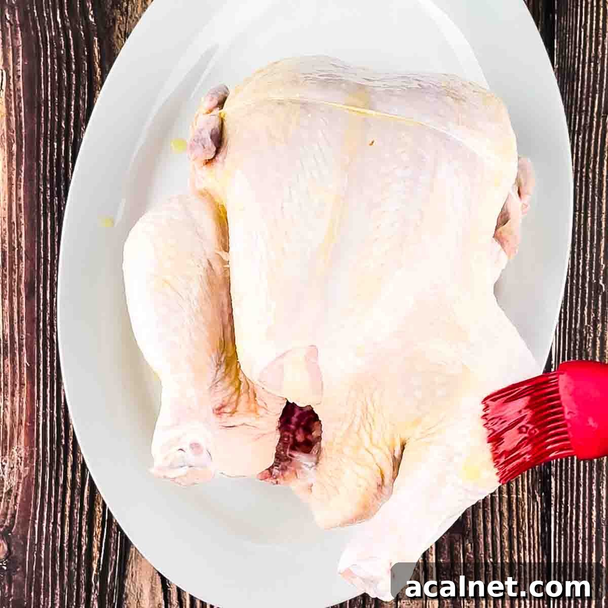 A red brush rubbing olive oil onto the outside of the chicken.