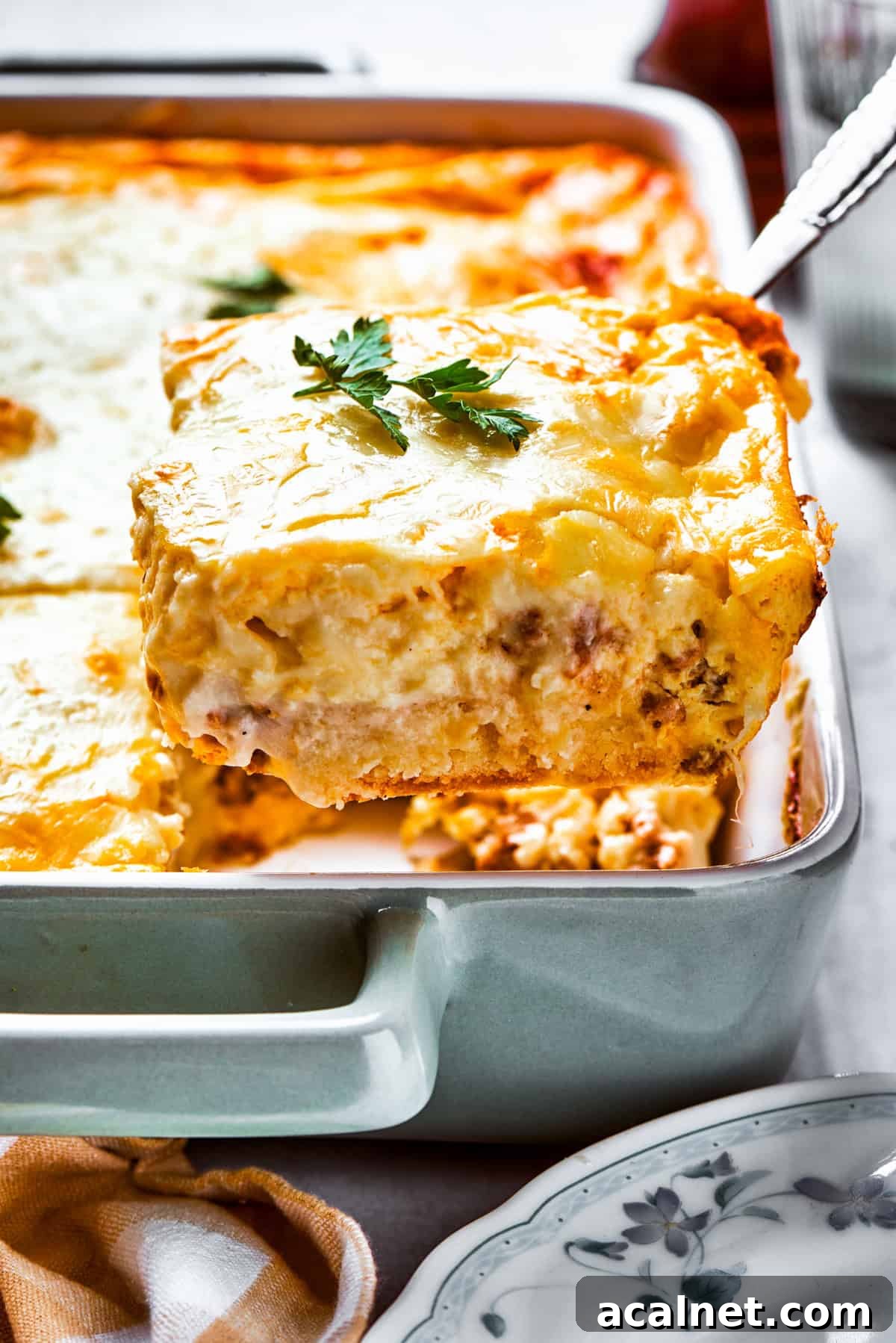 Biscuits and gravy casserole stars flaky biscuits, a rich and creamy sauce, and hearty sausage! Great for brunch or dinner! Lifting up a slice of biscuits and gravy casserole from a baking dish.