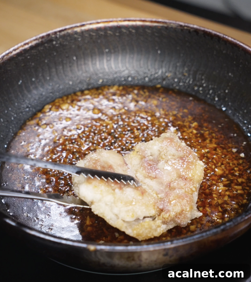 Fried chicken thighs are returned to the pan and tossed in the thickened honey garlic sauce until fully coated and glossy.