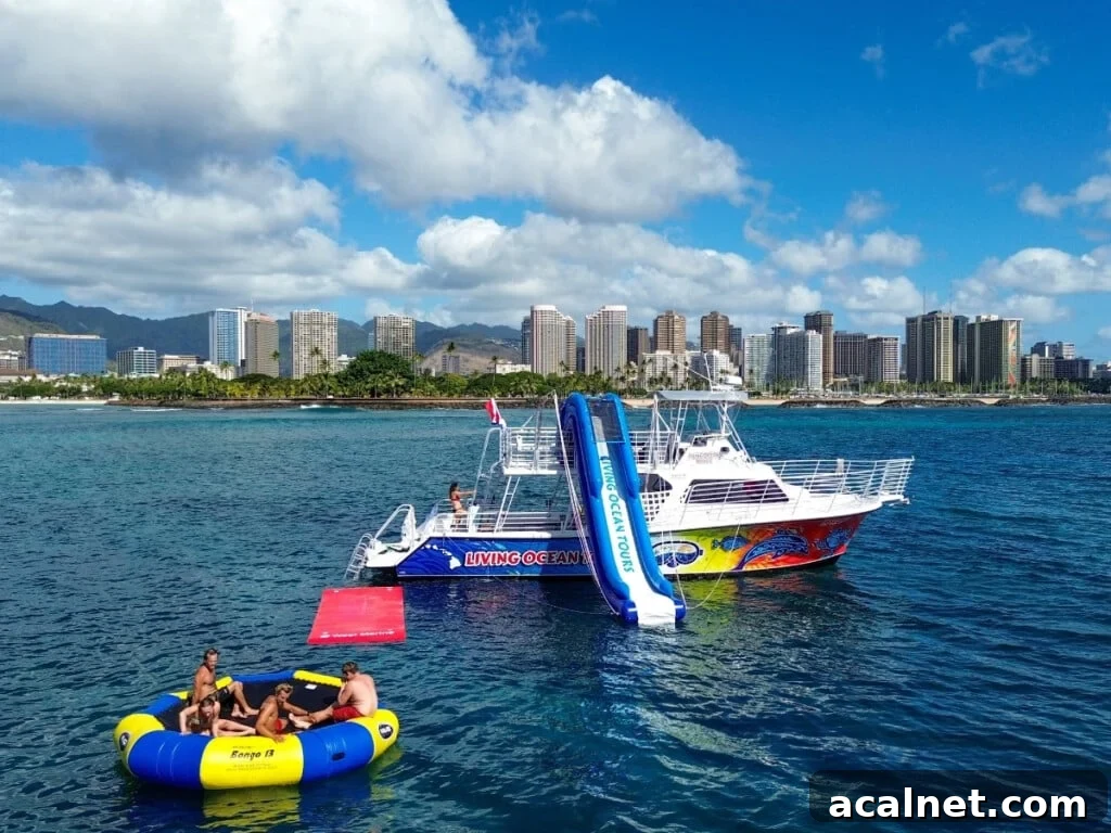 A recreational boat with waterslide and floating platform anchored off Waikīkī with city skyline and greenery in the background.