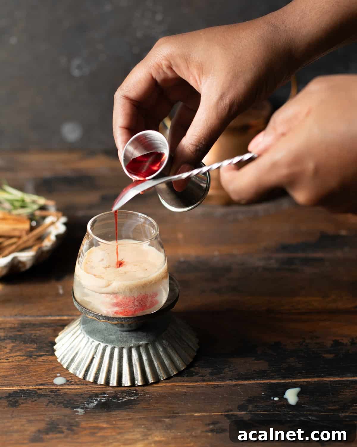 a hand pouring grenadine into a shot glass.