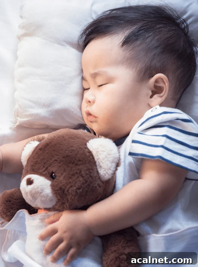 toddler in a striped shirt on a bed with a white pillow and sheets sleeping and cuddling a teddy bear - baby sleep