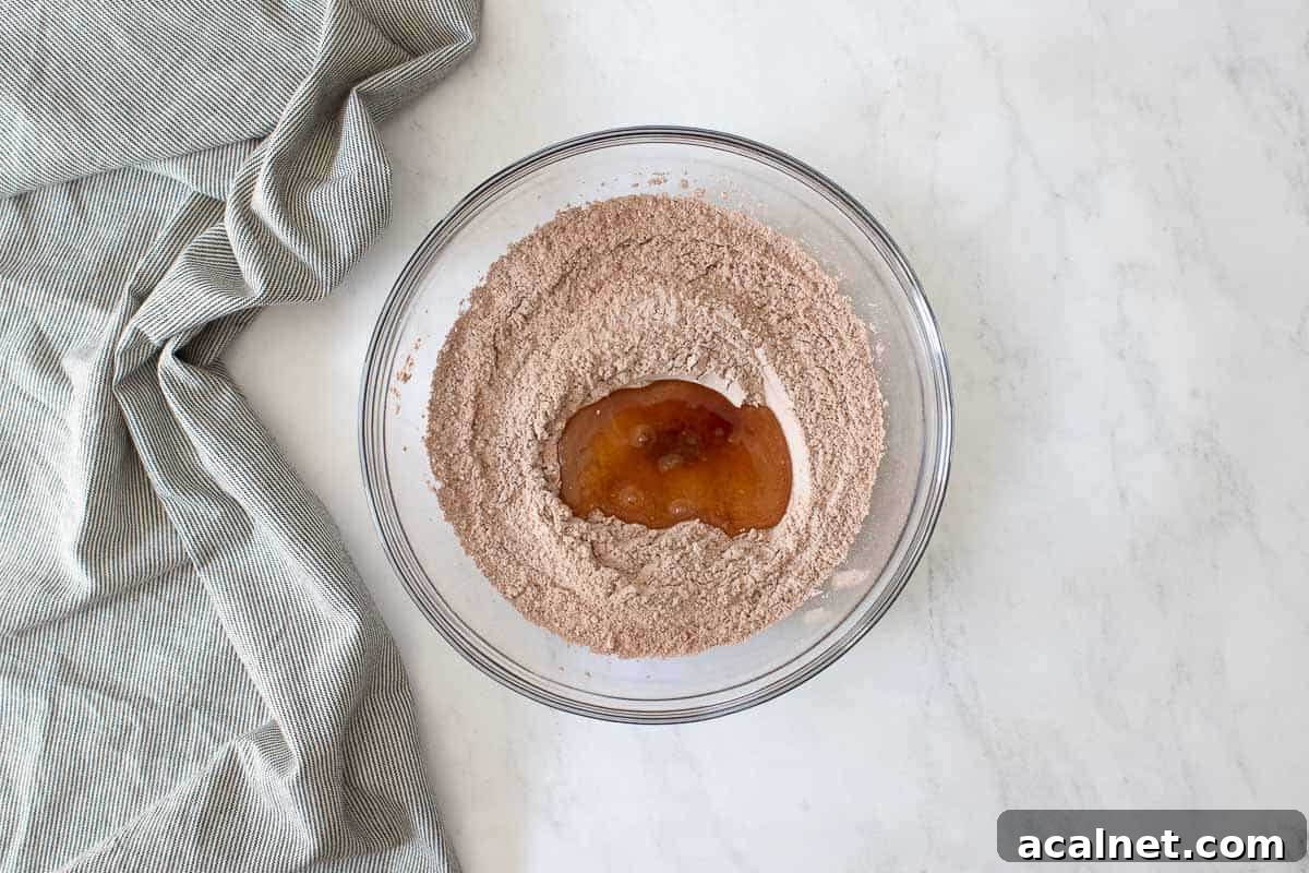Clear glass bowl with cocoa powder, egg whites and vanilla extract.
