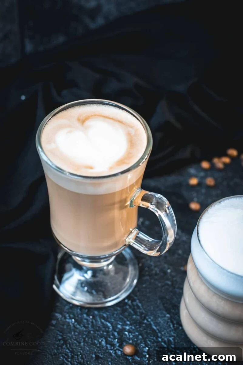 2 glasses filled with delicious vanilla latte. placed on dark ground. Left on has a latte art heart on top.