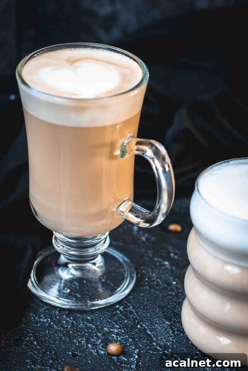 2 glasses filled with delicious vanilla latte. placed on dark ground. Left on has a latte art heart on top.