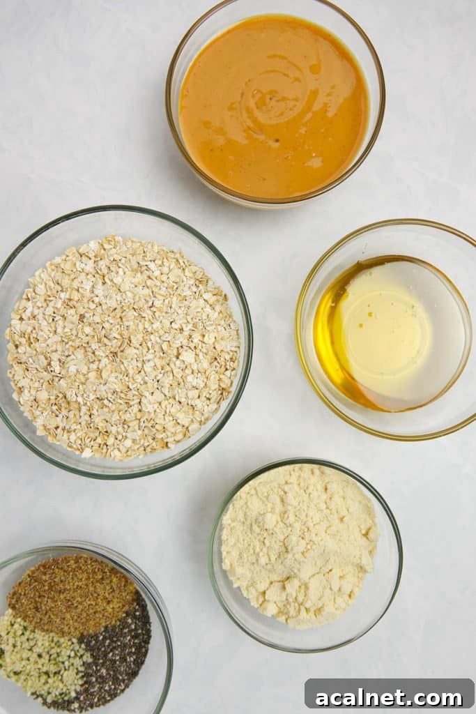 Peanut Butter Bliss Balls Recipe — No-Bake Snack Bites 3 Ingredients displayed in galss bowls on white marble counter. Ingredient include peanut butter, honey, oats, protein powder and seed blend.