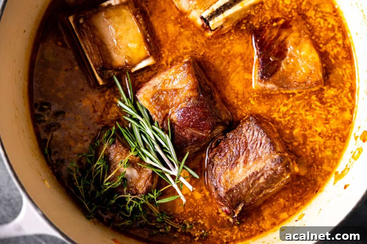 Short ribs in pan with sauce and fresh herbs.