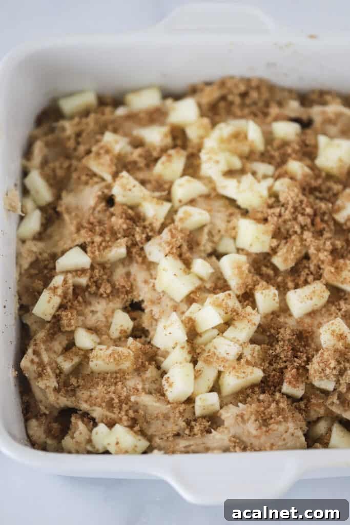 A square baking dish full of batter that's topped with apples and cinnamon sugar. 