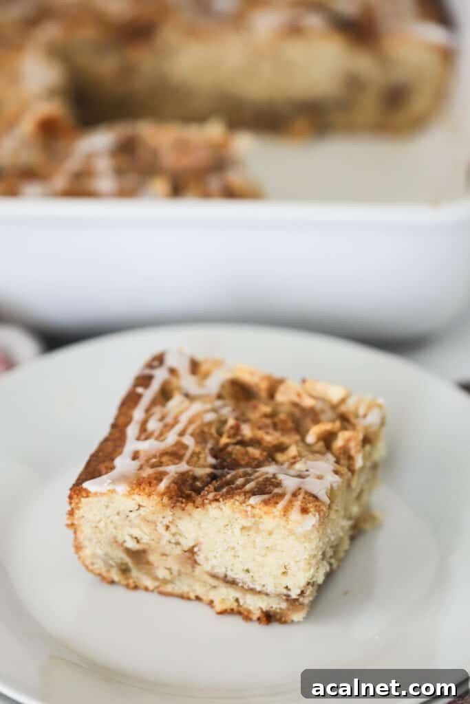 A slice of apple cinnamon coffee cake topped with glaze on a white plate.