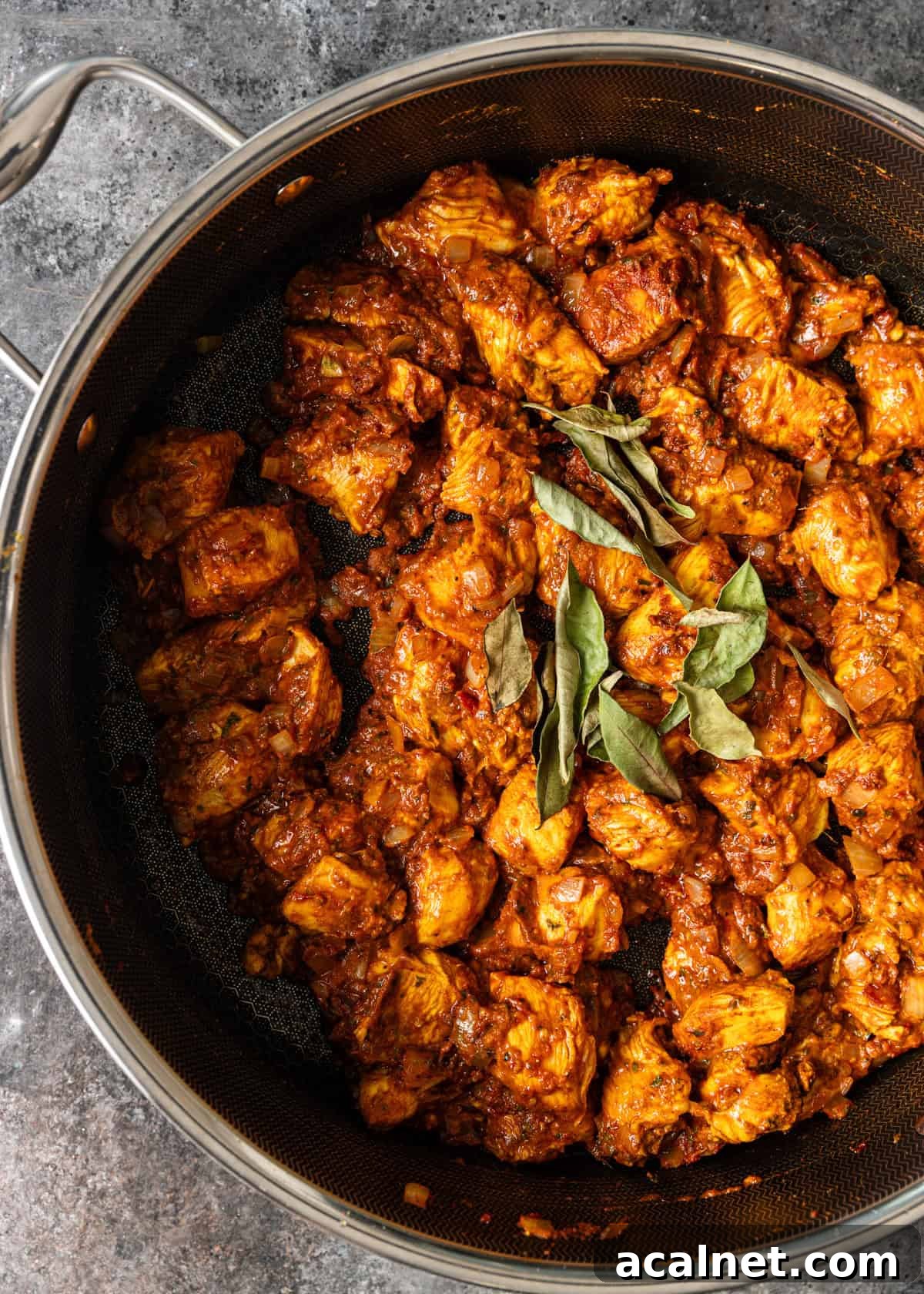 closeup overhead: chicken vindaloo in pan topped with curry leaves